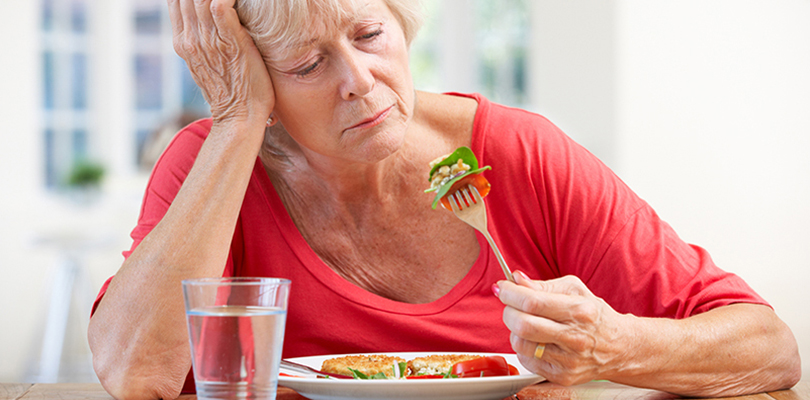 Older woman is playing with her food and expressing a loss in appetite in her face