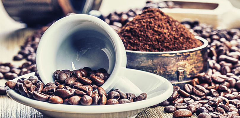 A cup of coffee beans, grounded and not grounded, sits on a counter