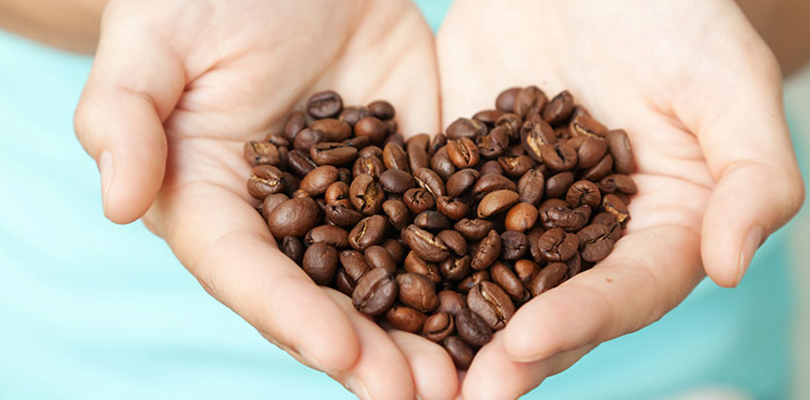 Hands holding coffee beans in the shape of a heart