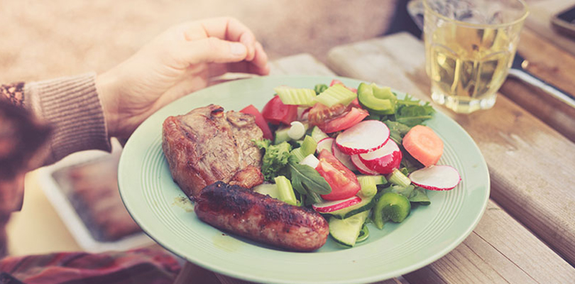 A meal is set out which includes a healthy salad, red meat, and drink