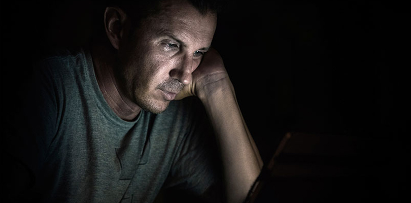 Man sitting in the dark looking at his laptop screen
