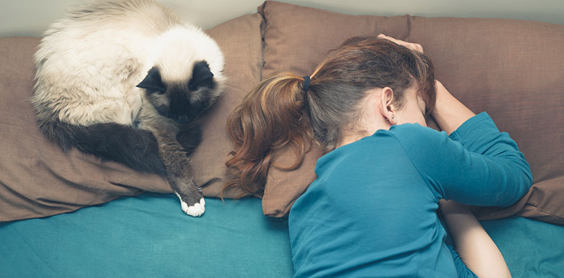 A woman is sleeping while her cat is sitting on a pillow beside her