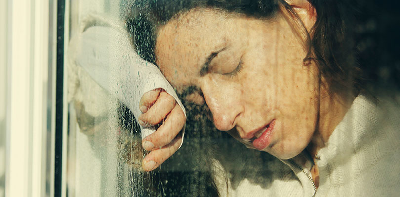 A woman is leaning on window glass looking sad