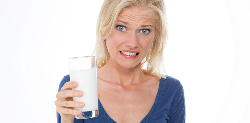 A woman is holding a glass of milk with a confused face