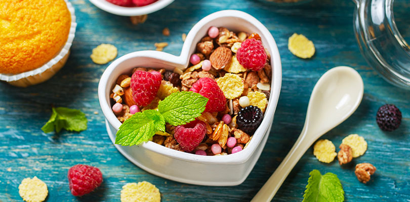 A yogurt and granola parfait is in a heart shaped bowl