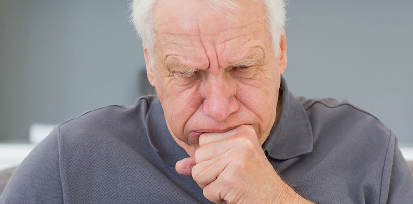 An older gentleman is coughing, one of the many symptoms of pneumonia