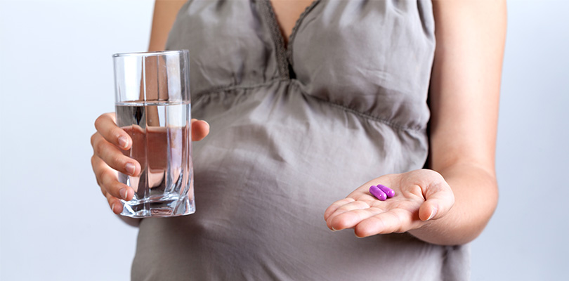 A pregnant woman is holding medicine in one hand and a glass of water in the other.