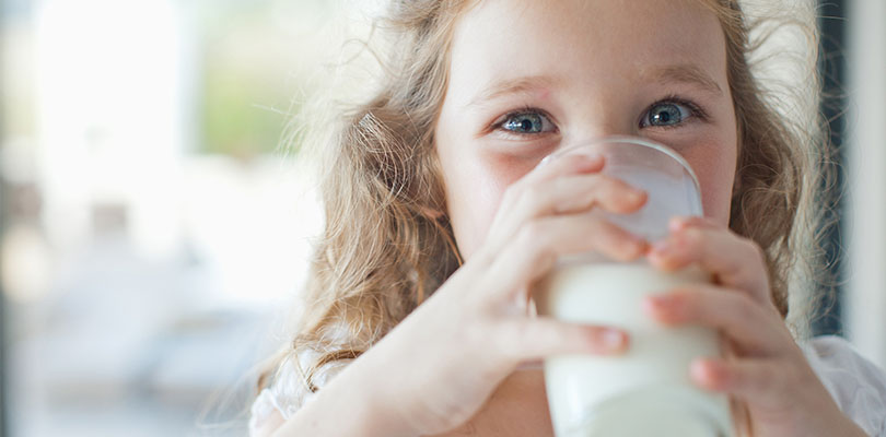 A young is drinking a glass of milk, which is a calcium-rich drink