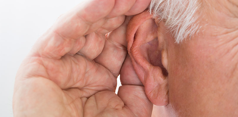 An older gentleman is cupping his ear
