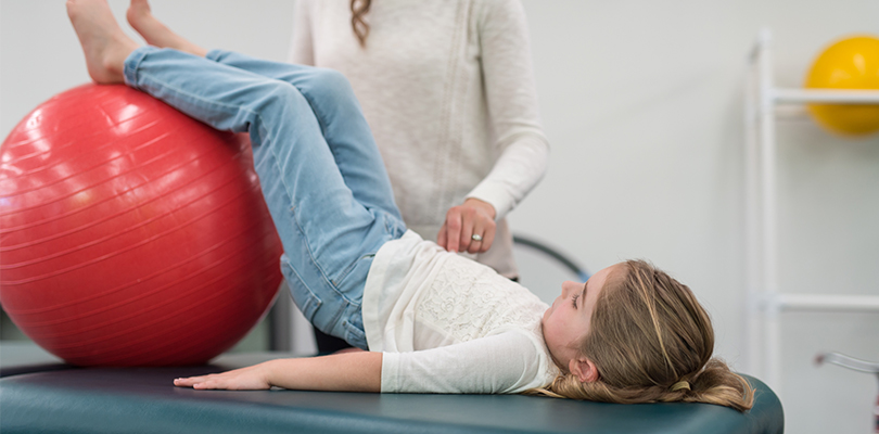 Young girl using exercise ball with physical therapist
