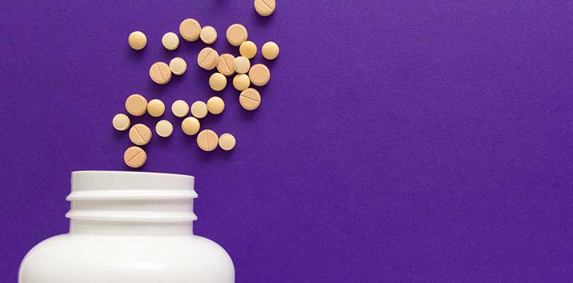 A bottle of pills spilling out onto a purple background