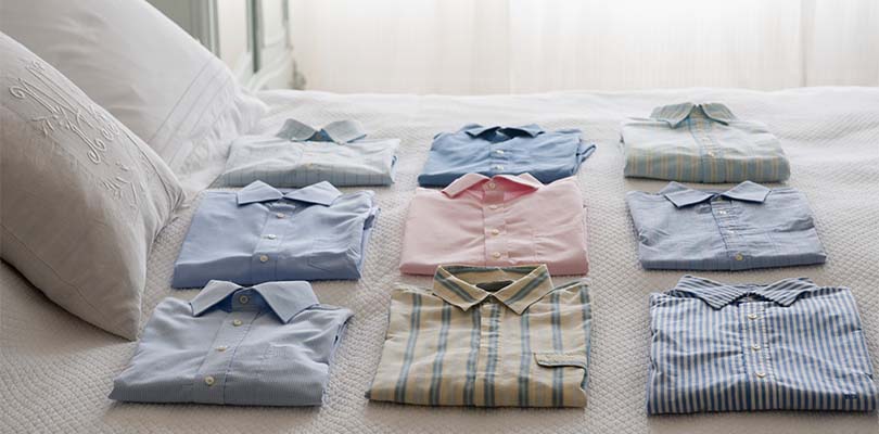 Folded dress shirts laying neatly on a bed.